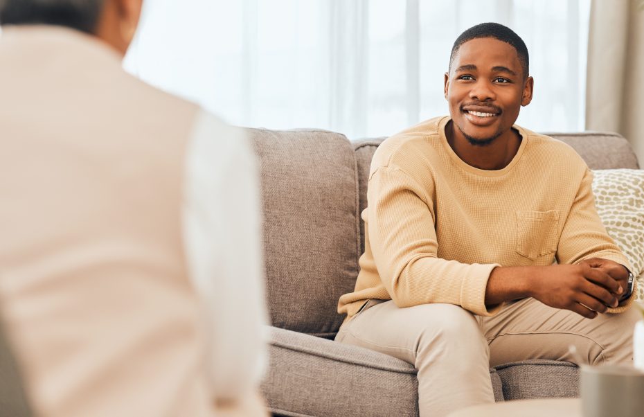 Man facing the camera sitting on sofa talking to someone facing away from the camera